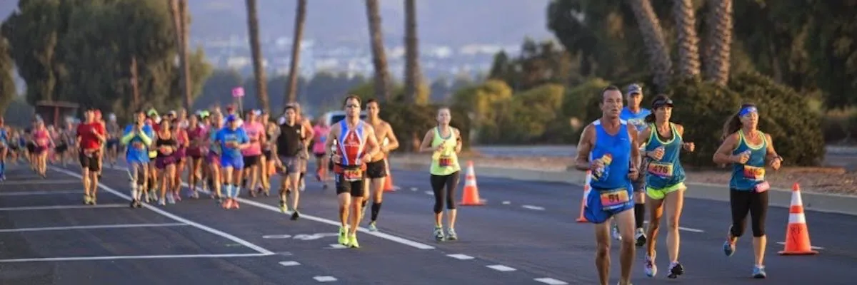 Runners participating in a road race, with palm trees and buildings in the background.