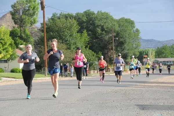 Runners on a road during a race, with trees and hills in the background.