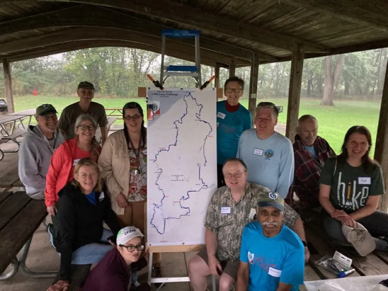 A group of people smiling and posing in front of a map of the Buckeye Trail Blue Blaze Challenge.