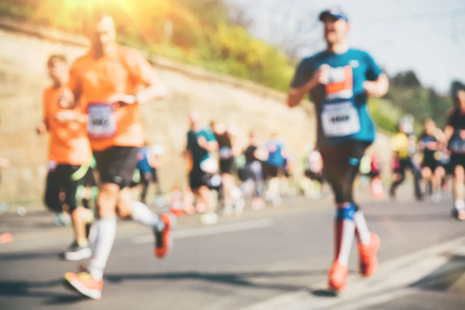 Runners in a race, with a focus on their legs and running shoes, under bright sunlight.