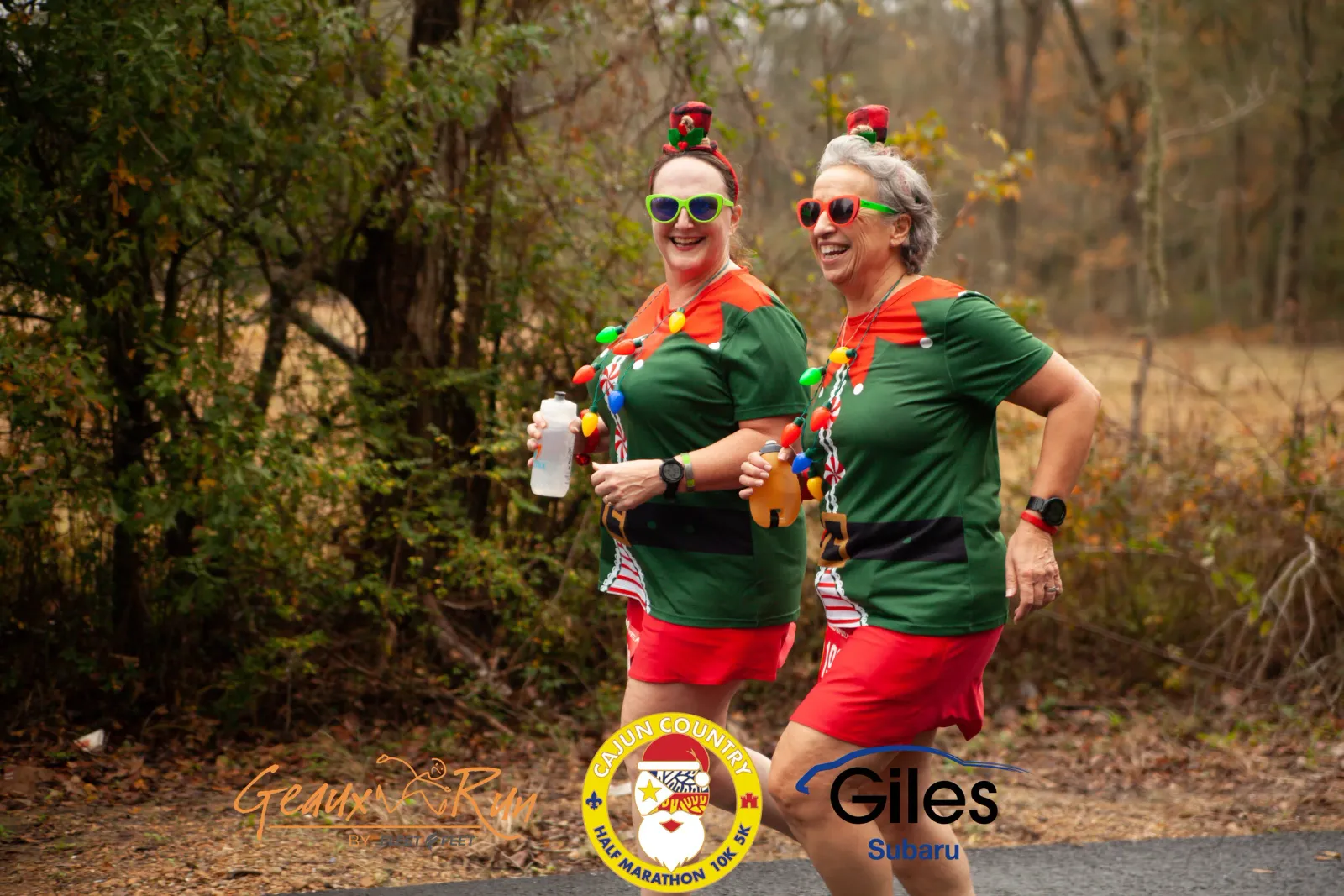 Two women in festive elf costumes with Christmas lights and red shorts running and smiling.