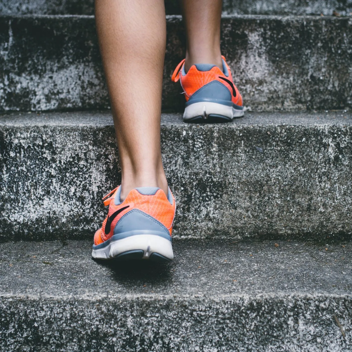 Close-up of a runner's legs and orange athletic shoes ascending concrete stairs.