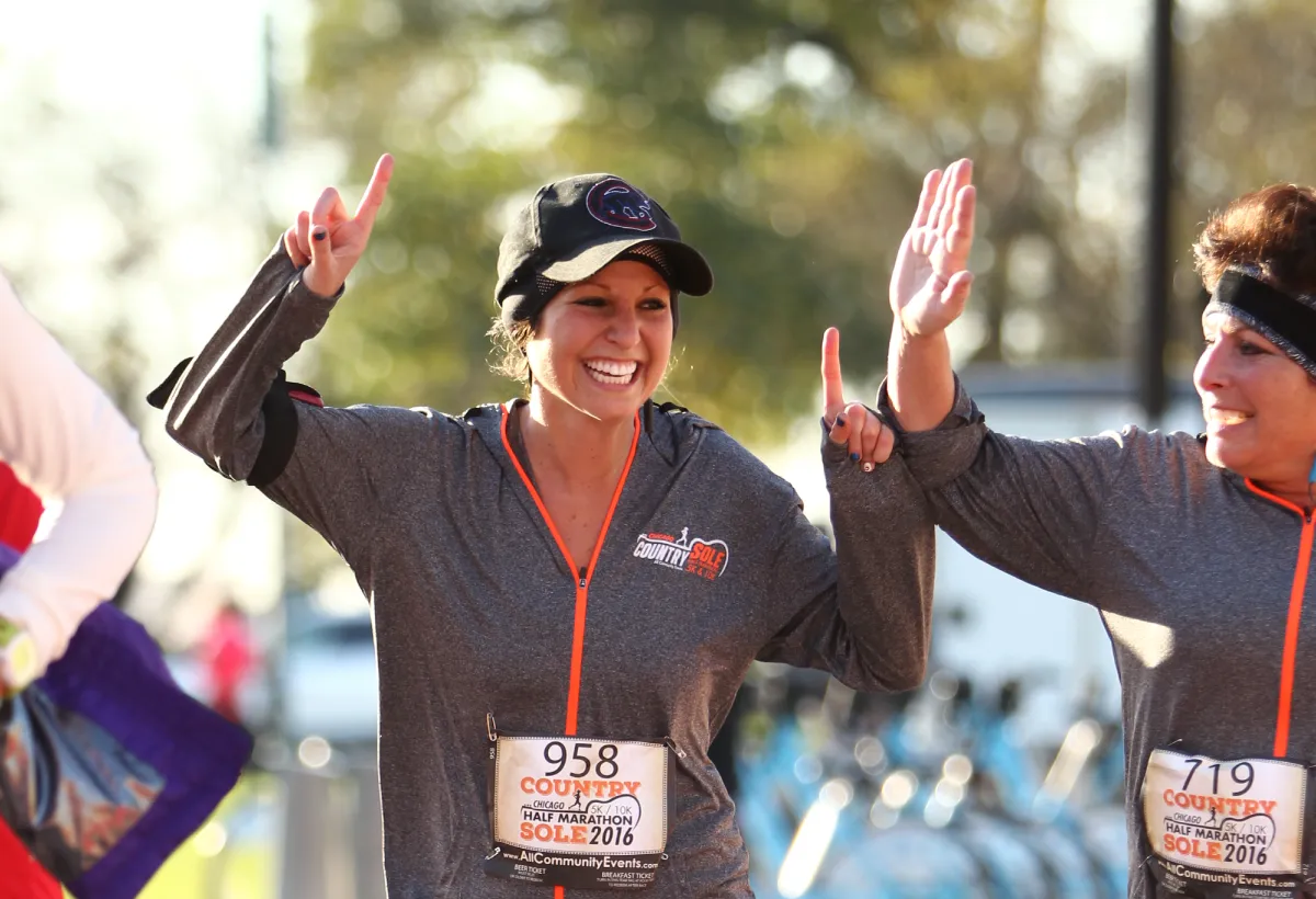 Two smiling women with their arms raised in celebration at a race.