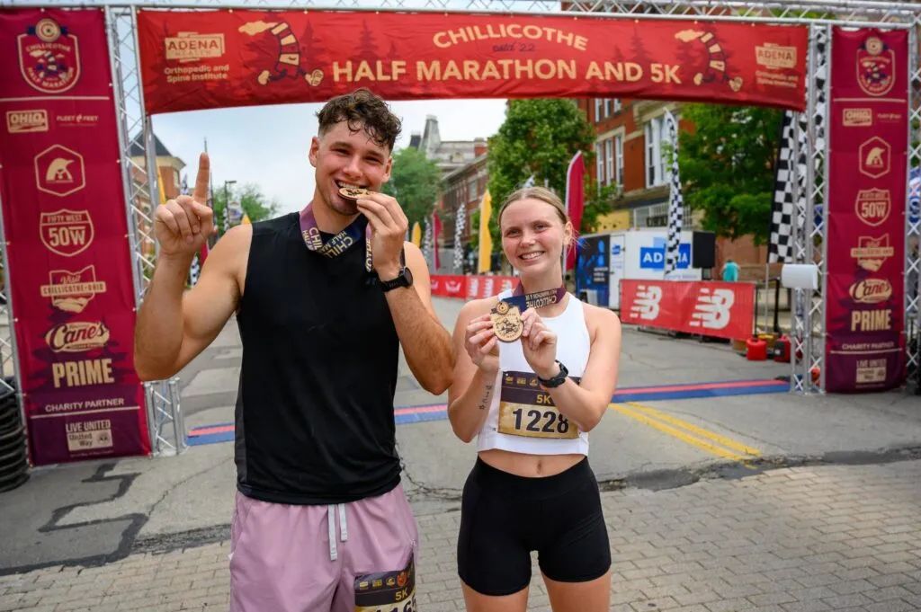 A smiling man and woman, both wearing race medals, stand at the finish line of the Chillicothe Half Marathon and 5K.