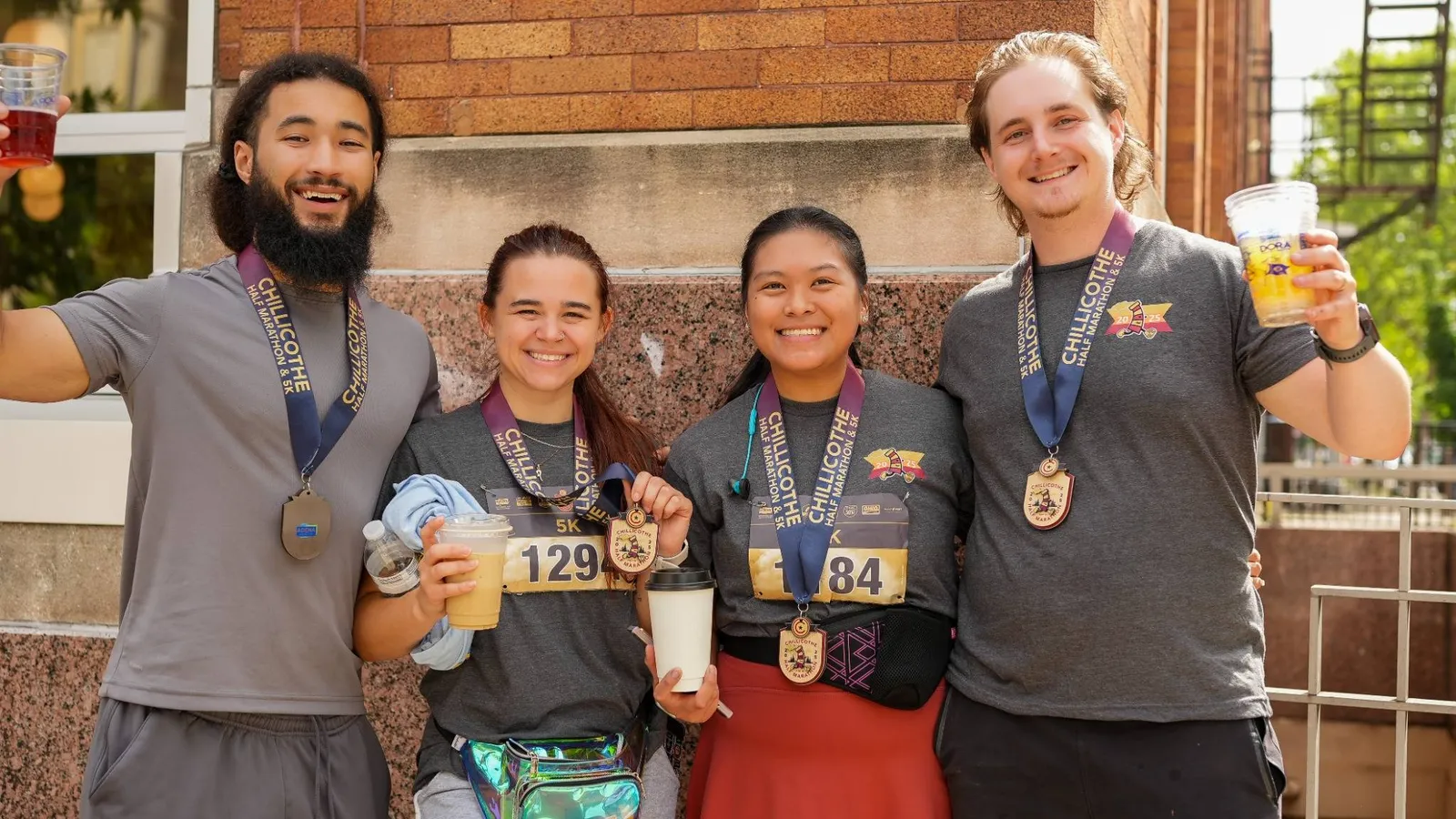 Four smiling runners, two men and two women, pose for a photo after completing the Chillicothe Half Marathon & 5K, all wearing their race medals and holding drinks.