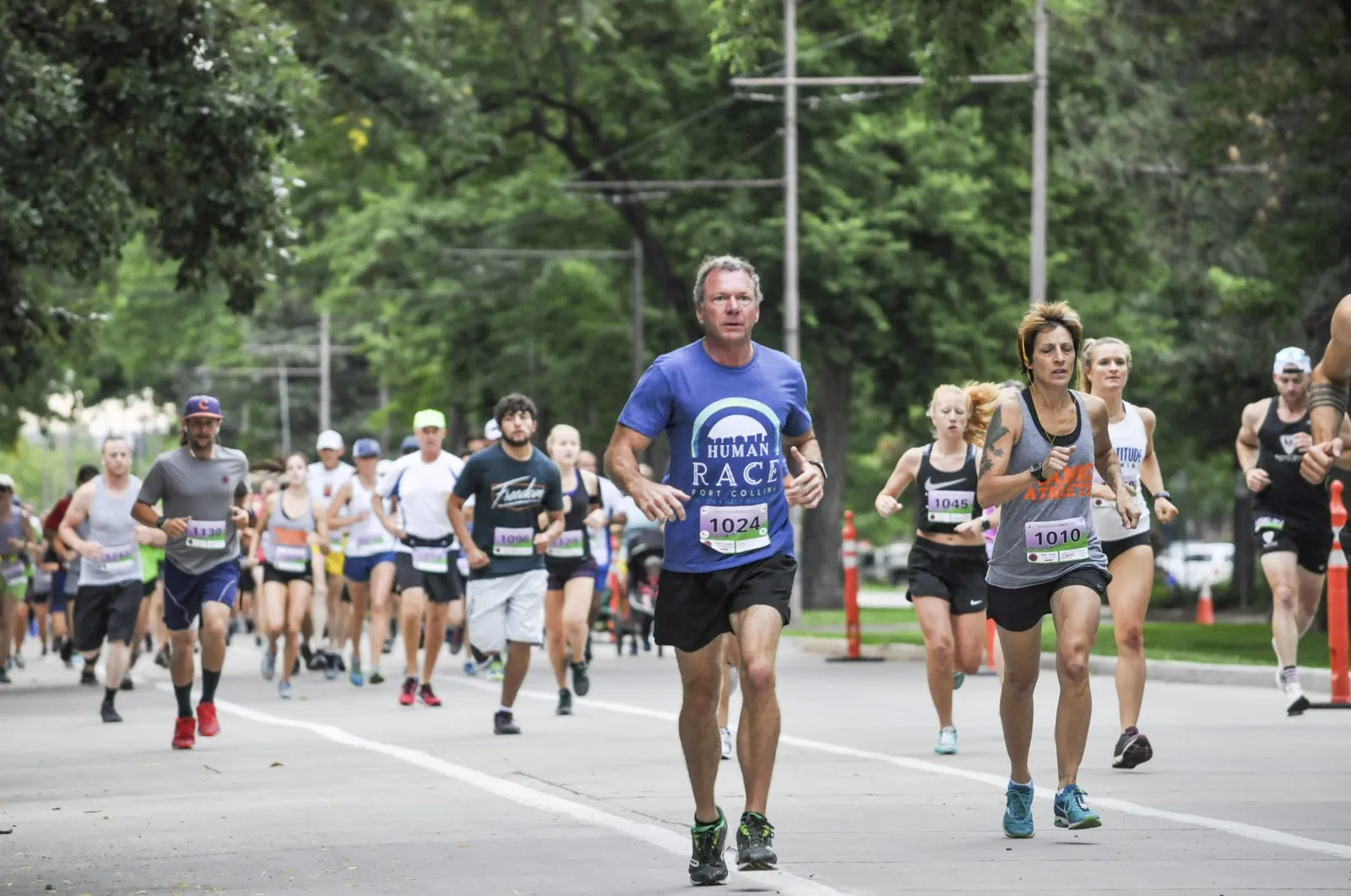 Runners on a paved road during a race, with trees lining the sides of the course.