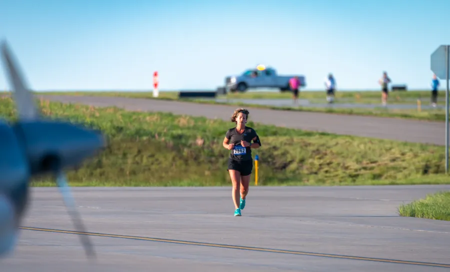 A female runner with bib number 2862 runs on a paved road with grass and a clear blue sky in the background.