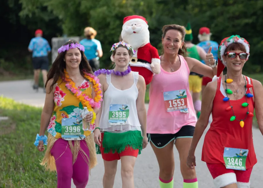 Runners in festive Christmas and Hawaiian-themed costumes participate in a race, smiling and enjoying the event.