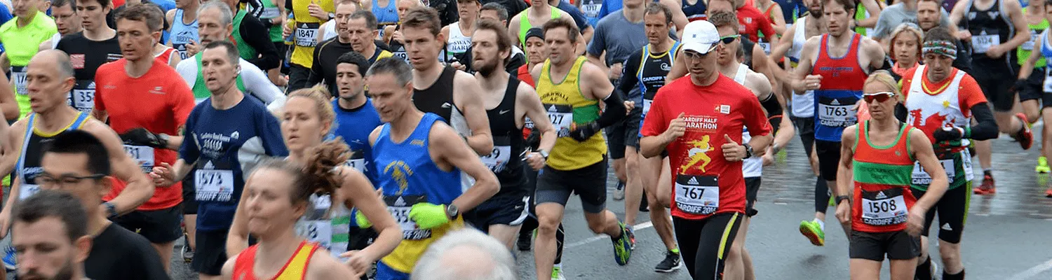 A large group of runners in various colored racing attire running together on a road during a race.