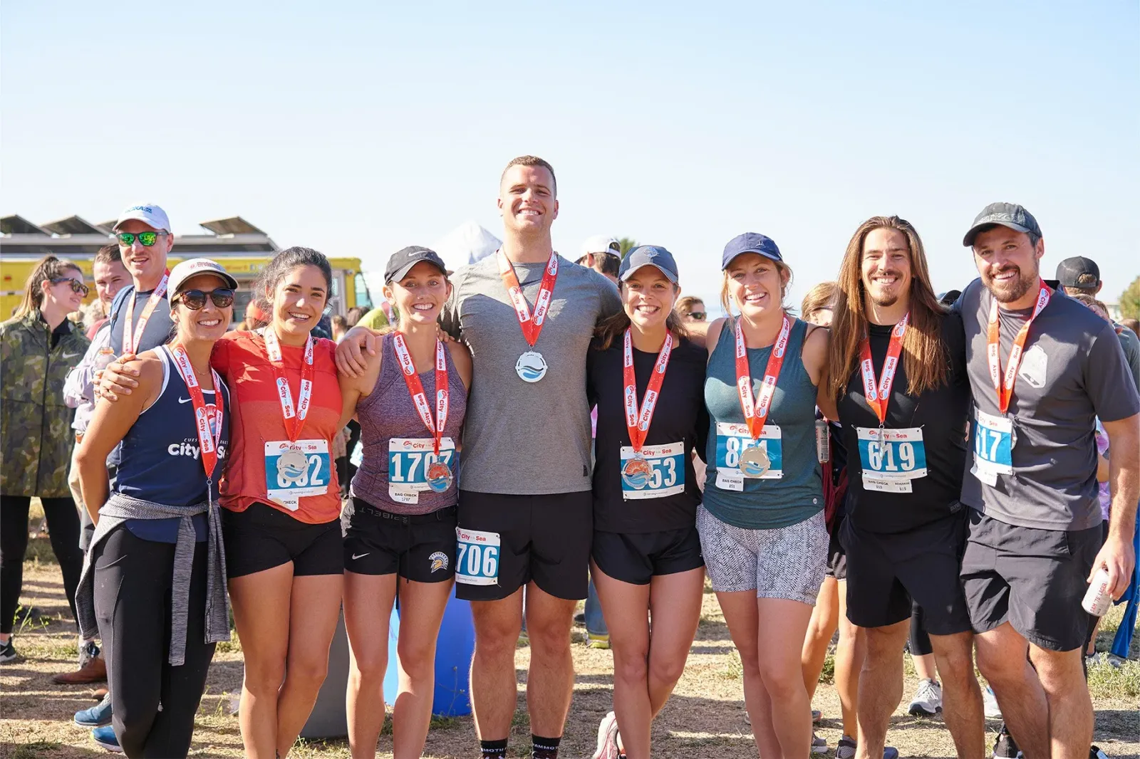 A group of smiling runners, some wearing medals, pose for a photo after completing the City to the Sea Half Marathon.