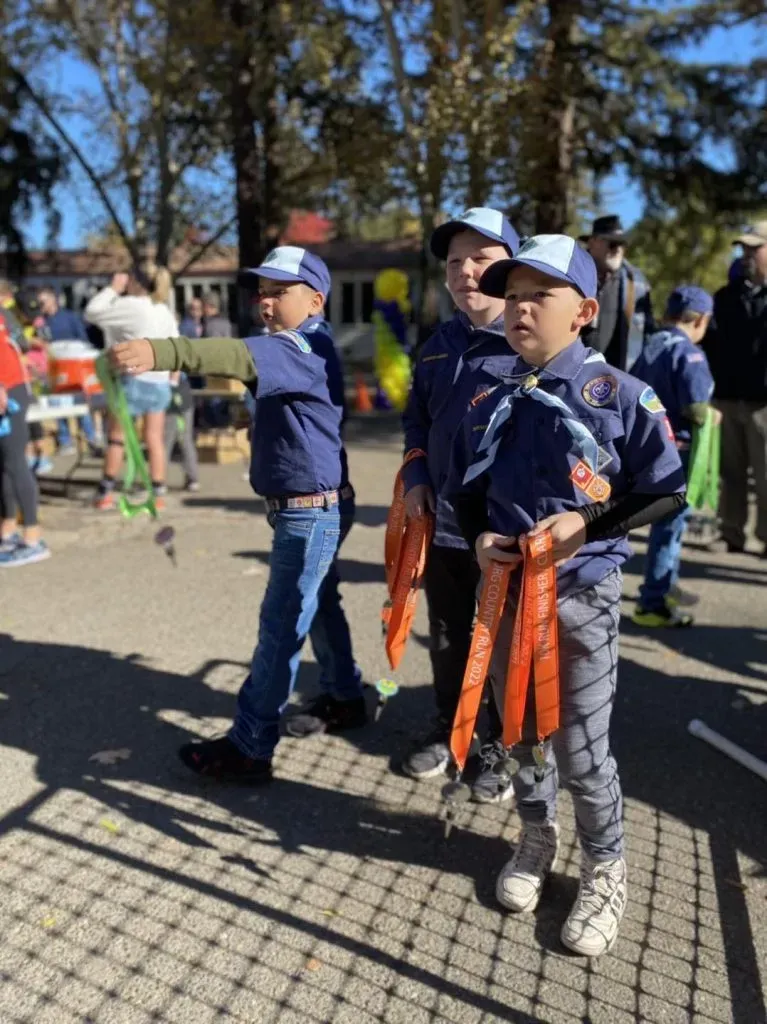 Young participants in scout uniforms holding finisher medals at a race event.