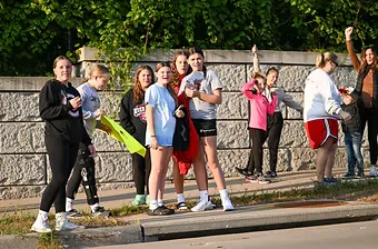 A group of young people, some smiling and posing, stand by the side of a road, appearing to be at the start of a race.