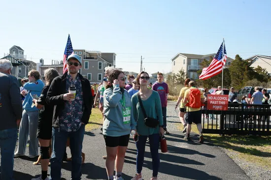 A group of people gathered outdoors, some wearing race bibs, with American flags and houses in the background.