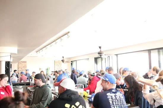 A crowd of people wearing hats and casual clothing gathered indoors, possibly at a race event registration or social gathering.