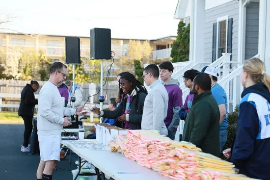 People queuing at a table to collect race packets, with volunteers handing out items.