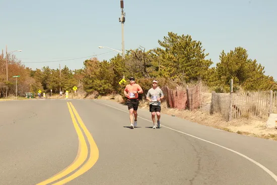 Two runners on a road with trees and a fence in the background.