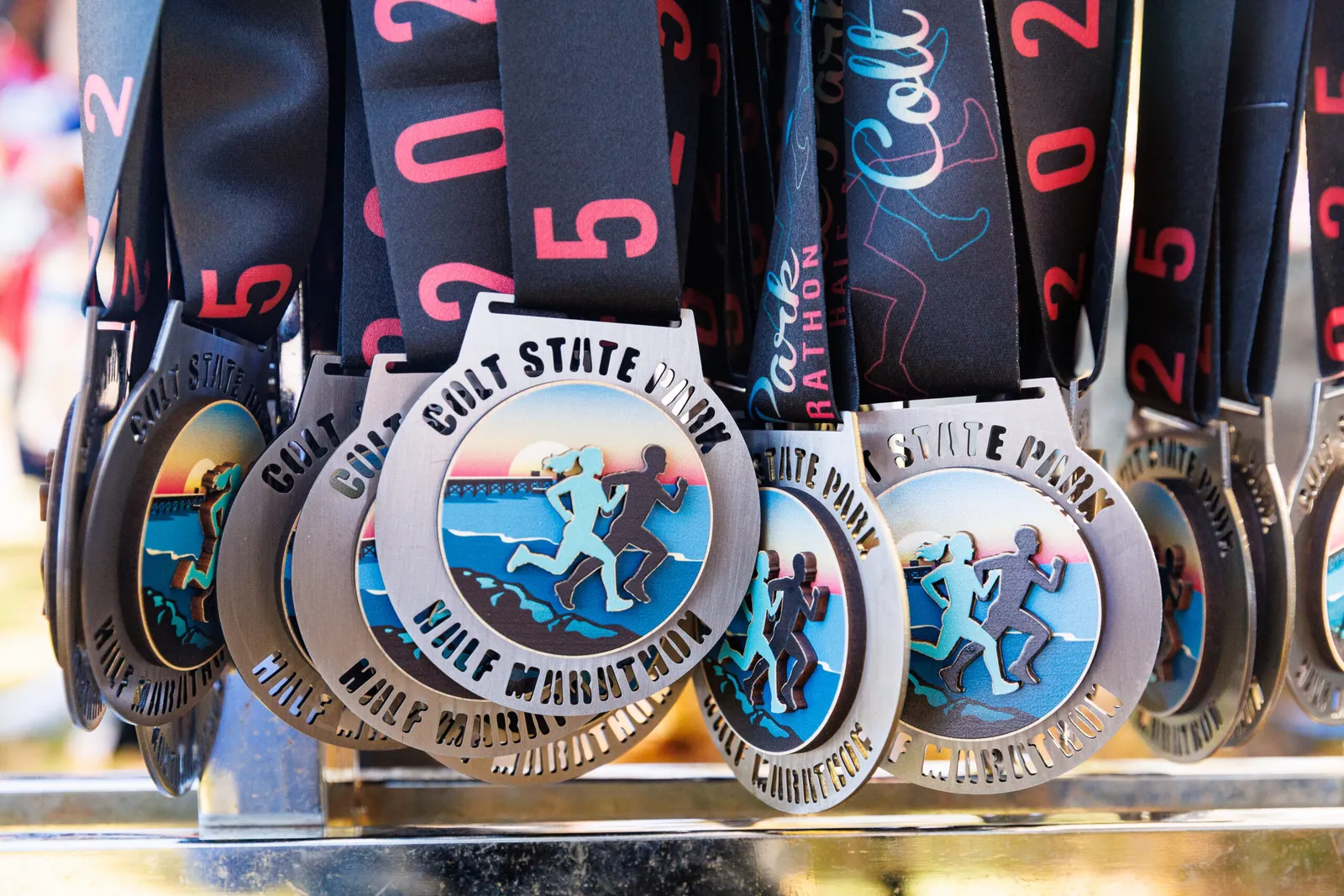 A close-up view of several race medals hanging, each featuring a graphic of runners by the water with a sunset and bridge in the background.