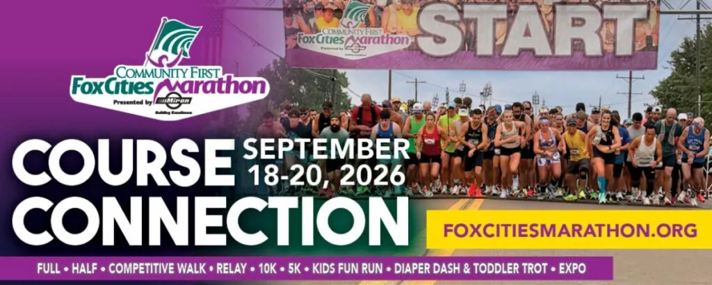 A large group of runners at the start line of the Fox Cities Marathon, with a banner overhead that reads 'START'.