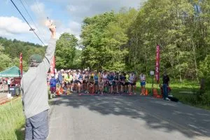 Runners lined up at the start line of the Covered Bridges Half Marathon, with a race official raising their arm.