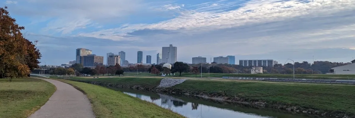 A scenic view of a city skyline with a river and a paved path in the foreground, suggesting a race course.