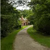 A winding gravel path through a lush green forest leads to a small brick building with a chimney.