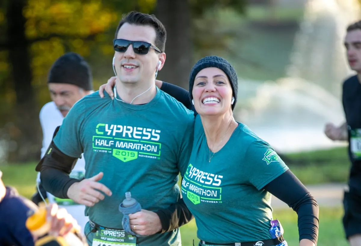A smiling couple running a race, both wearing Cypress Half Marathon shirts.