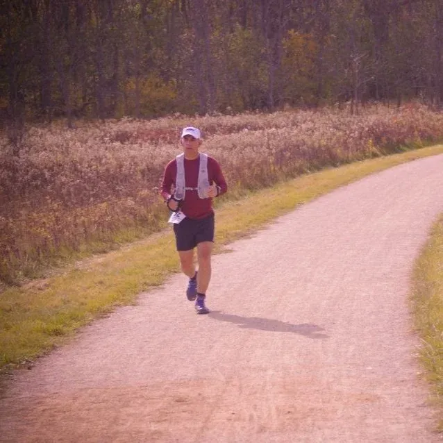 A runner on a dirt path with trees in the background.
