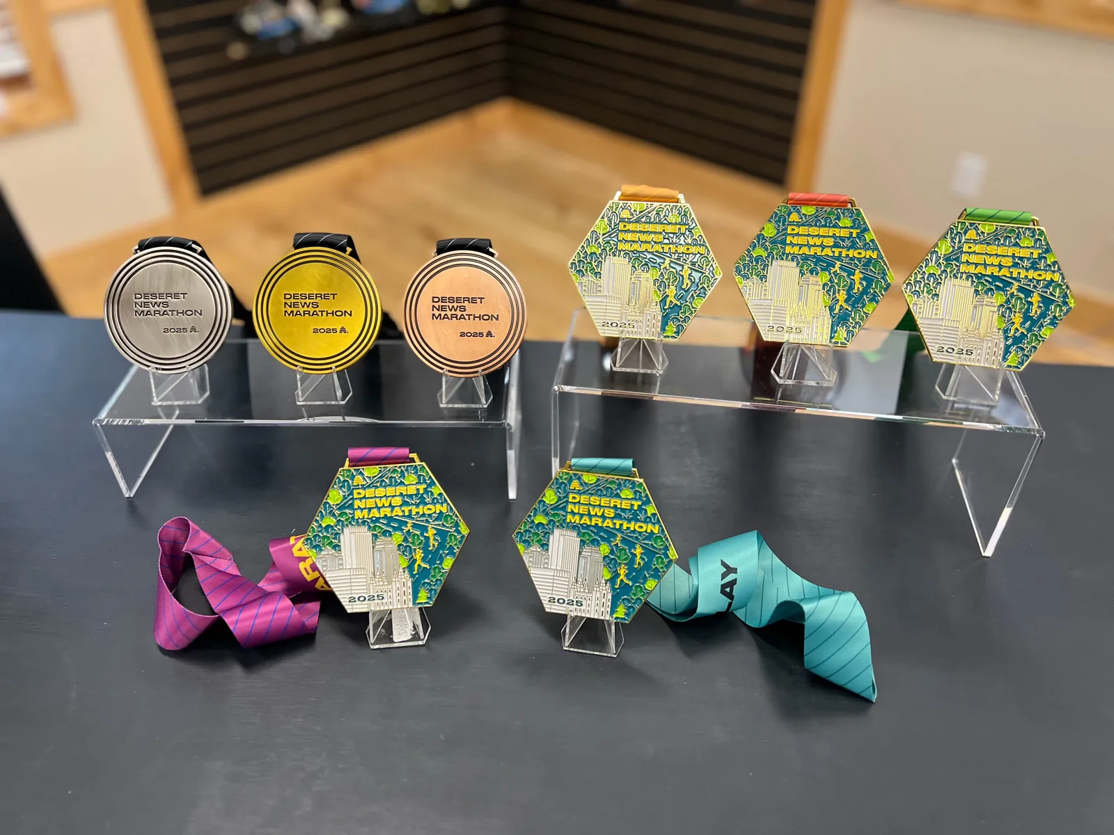 A display of various Deseret News Marathon medals from 2025, including silver, gold, and bronze variations, with colorful ribbons.