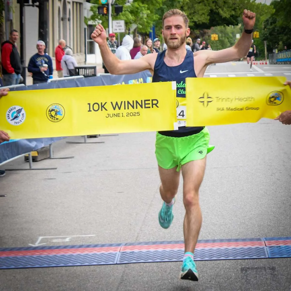 Male runner celebrating as he crosses the finish line, breaking through a '10K WINNER' banner.