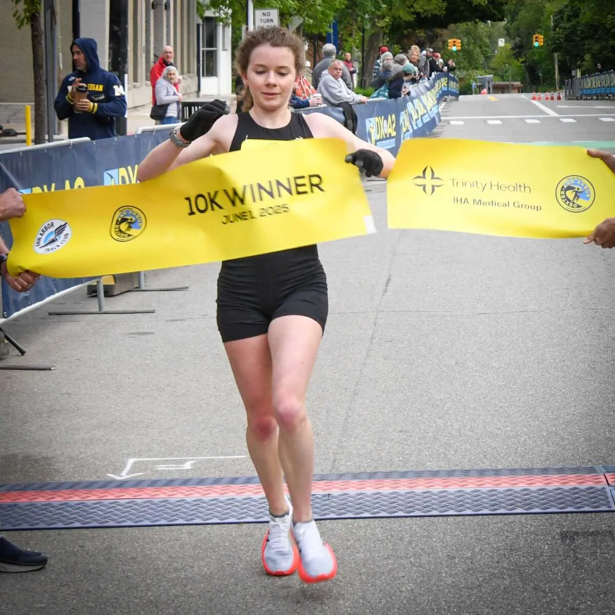 Female runner crossing the finish line holding a '10K WINNER' banner.