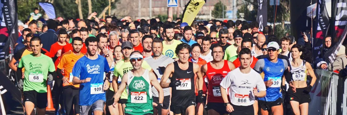 A large group of runners at the start line of a race, with many participants visible in the foreground and background.