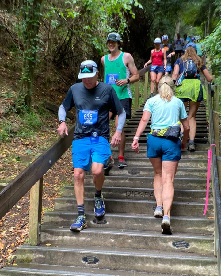 Runners ascending a wooden staircase during a race, with lush greenery on either side.