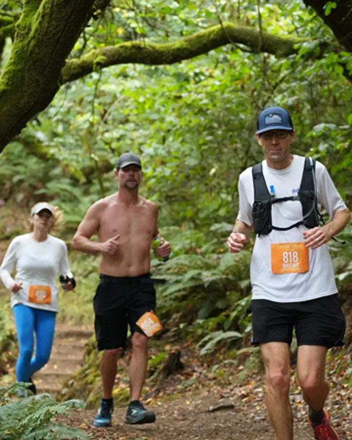Three runners on a wooded trail, two men and one woman, with bib numbers visible.
