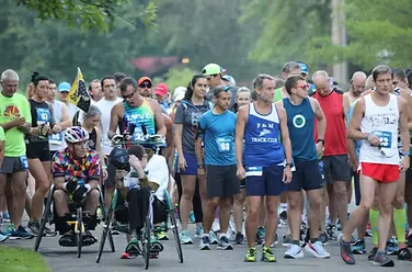 A group of runners and participants in wheelchairs line up at the start of a race.
