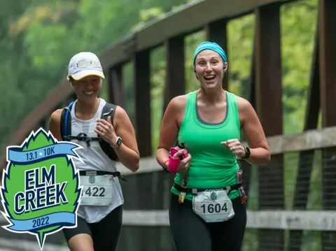 Two female runners smiling as they run across a bridge during the Elm Creek 13.1K race in 2022.