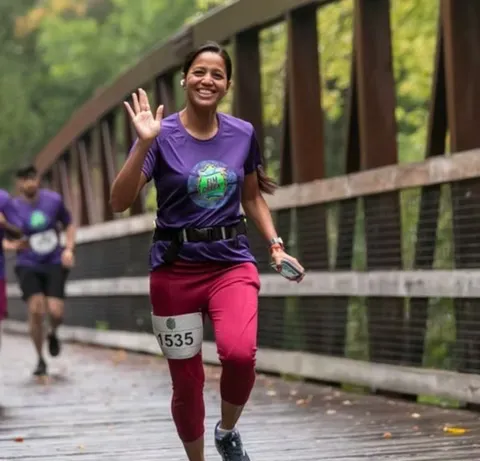 A female runner smiles and waves while running across a wooden bridge during a race.