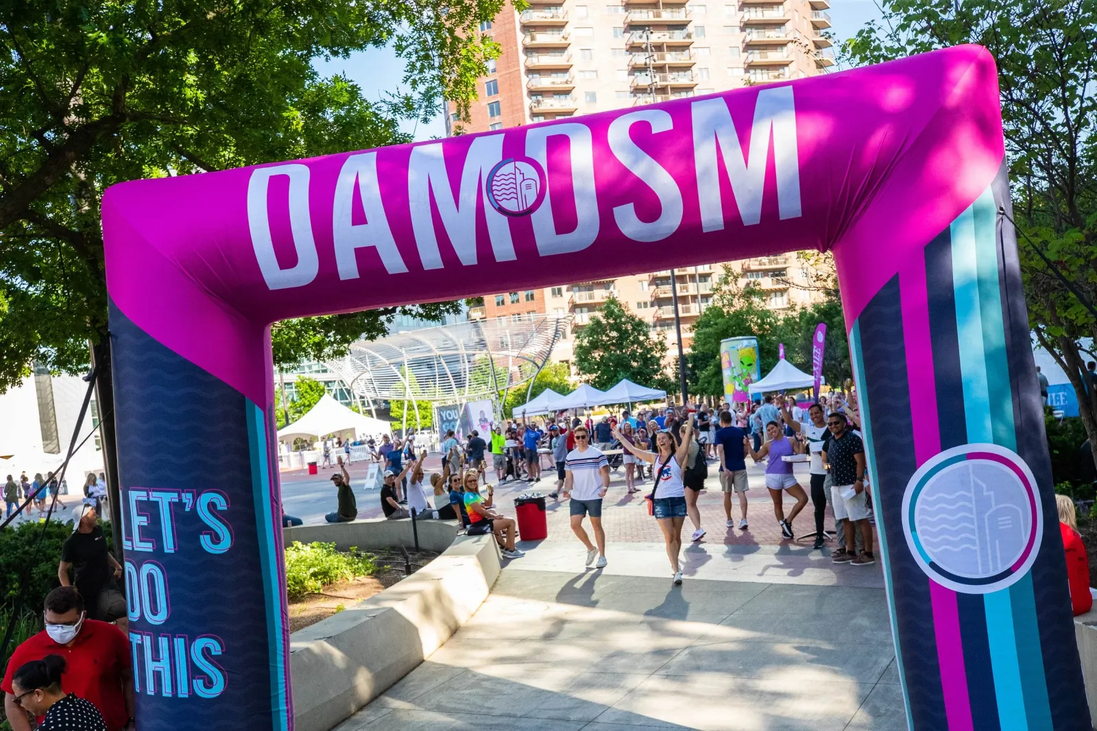 A group of people celebrating under a large inflatable archway with 'DAMtoDSM' written on it.