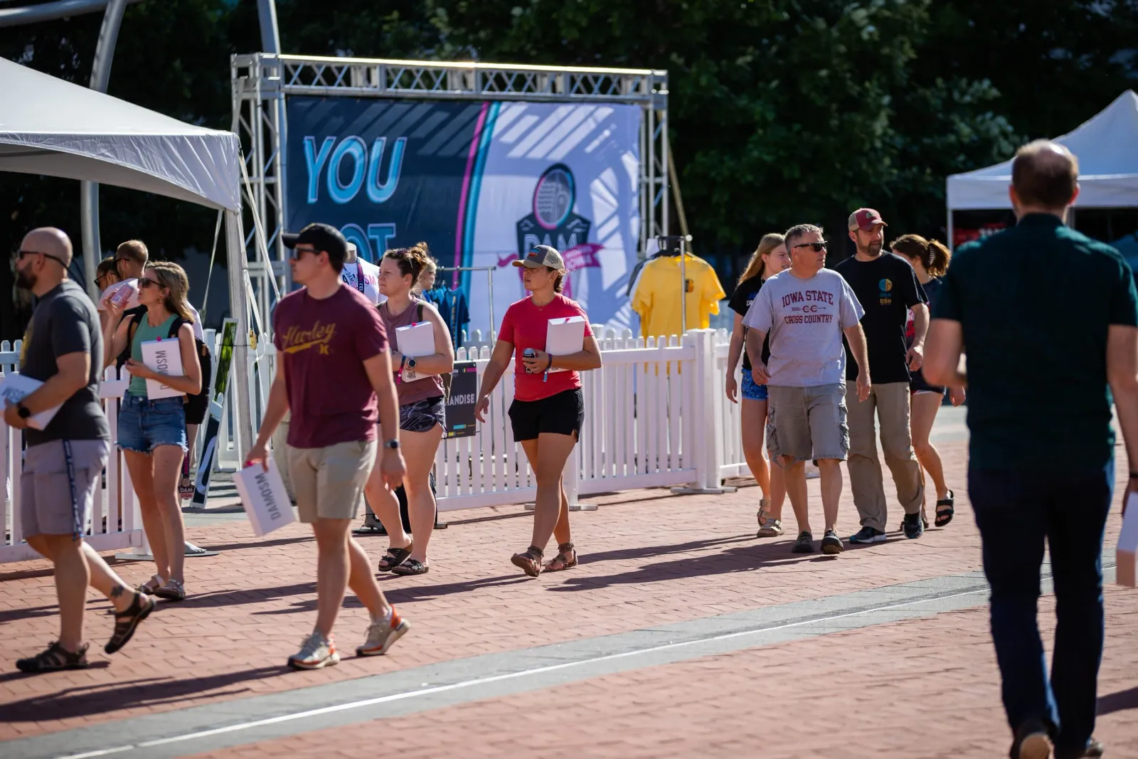 People walking past tents and a banner at a race event, some carrying packets.