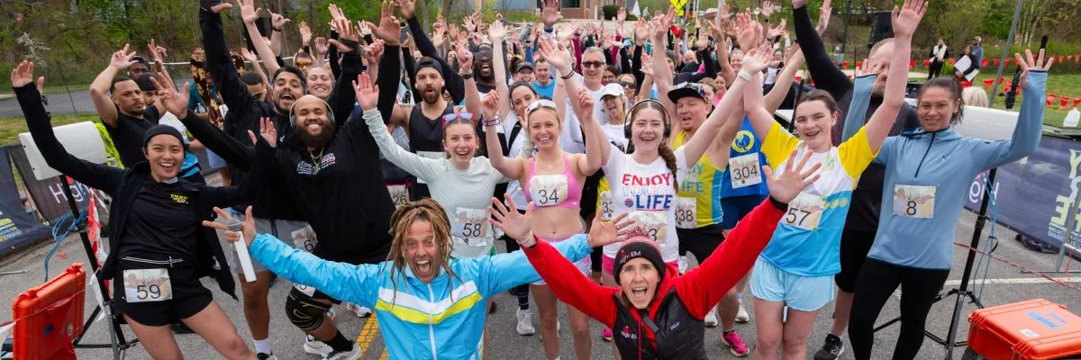 A large group of runners with their arms raised in celebration at a race start or finish line.