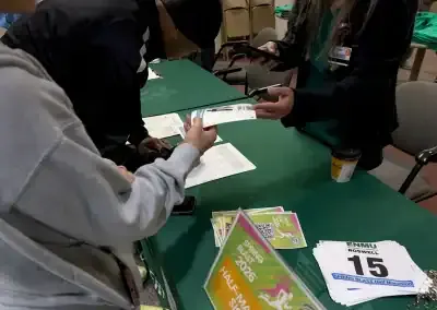 People picking up race bibs and materials at a registration table.