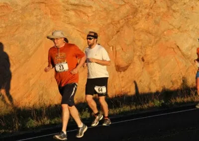 Two runners on a road with a large rock formation in the background.