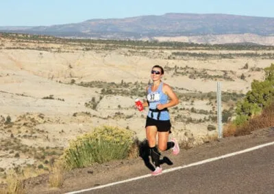 A female runner with bib number 37 runs on a road with a scenic desert landscape in the background.