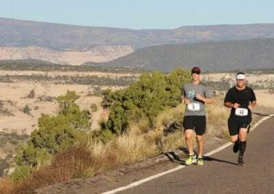 Two runners on a road with a scenic desert landscape in the background.