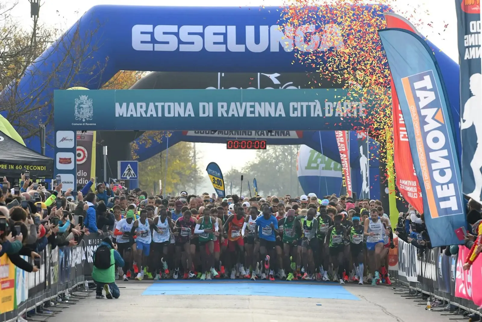 Runners starting a marathon under an archway with confetti falling.