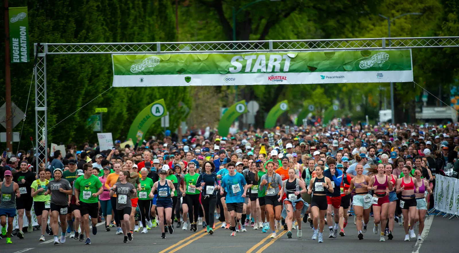 A large group of runners at the start line of the Eugene Marathon, with a banner overhead that reads "START".