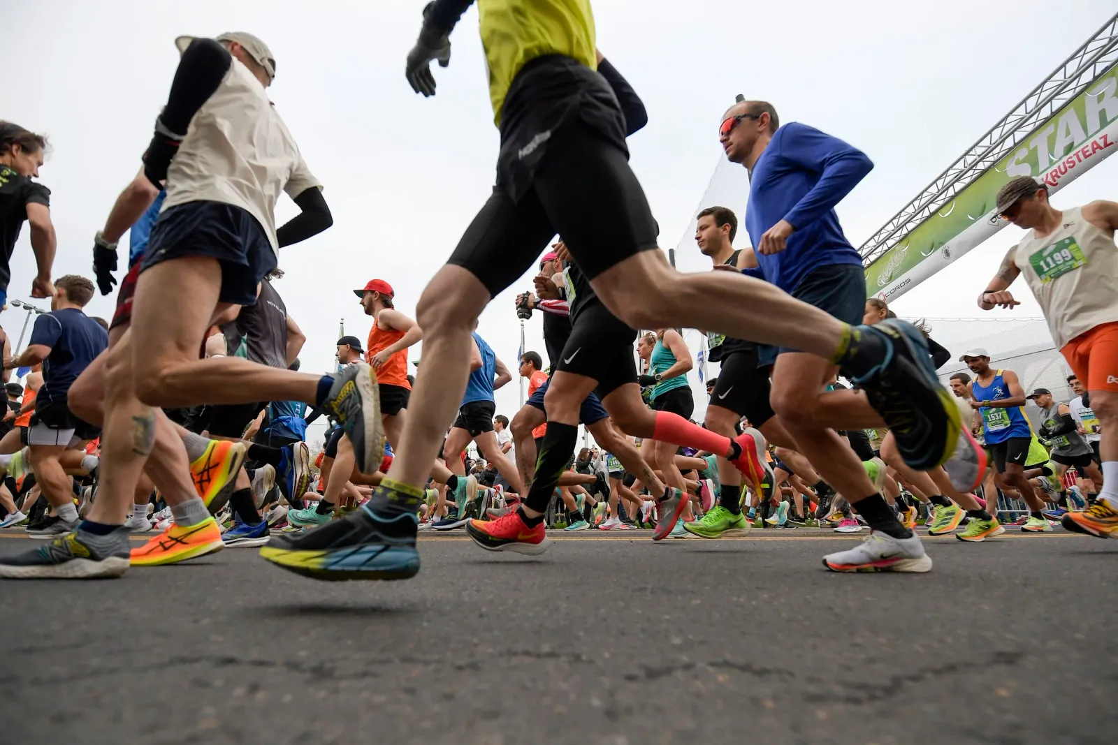 A group of runners in motion at the start line of a race, with a banner overhead that reads 'START'.