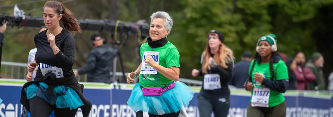 Runners in a race, some wearing tutus, with bib numbers visible.