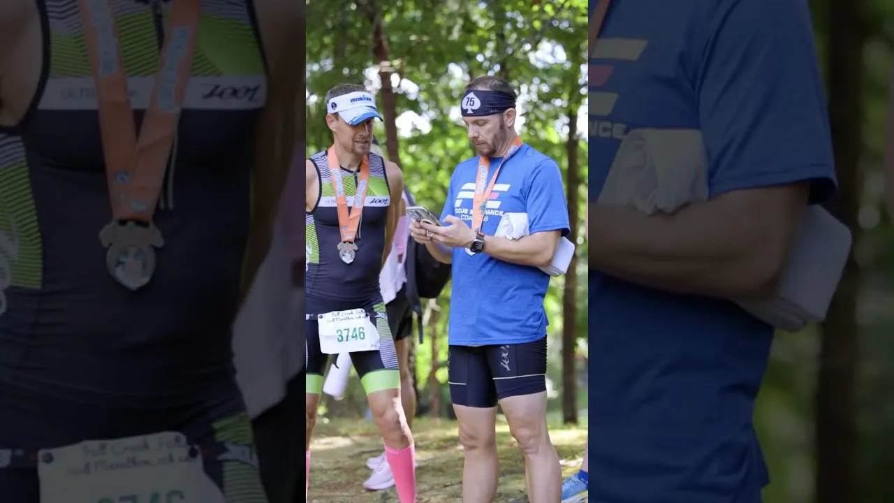 Two runners wearing medals, one looking at his phone, in an outdoor setting.