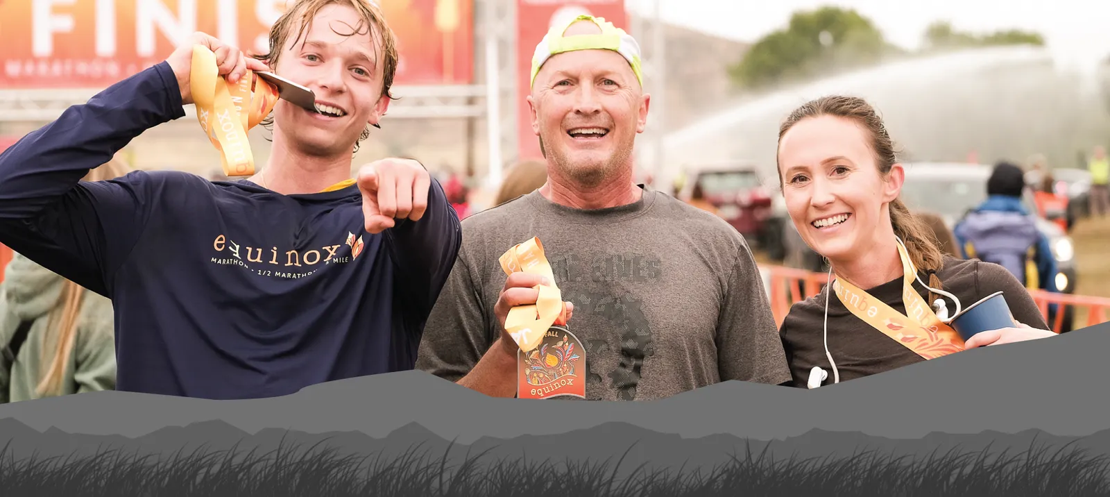 Three smiling runners, two men and one woman, proudly display their race medals at the finish line of the Fall Equinox Marathon.