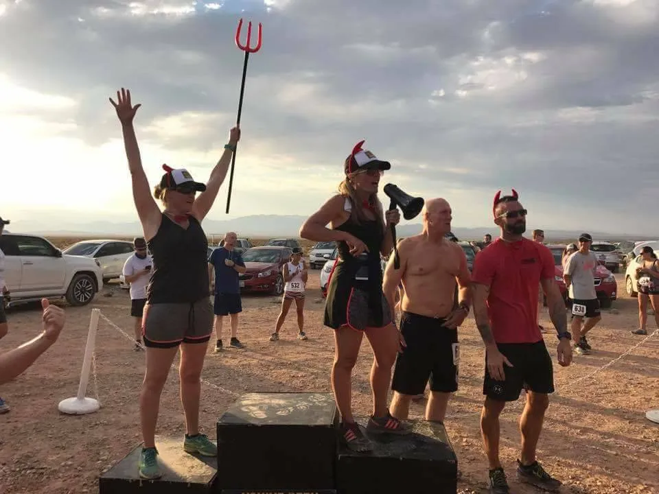 People celebrating at a race, one person holding a trident and wearing devil horns.